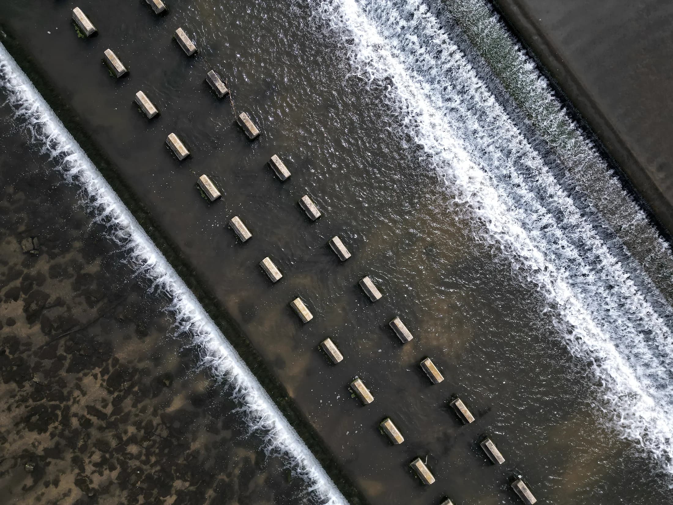 An aerial view of water flowing over a weir.