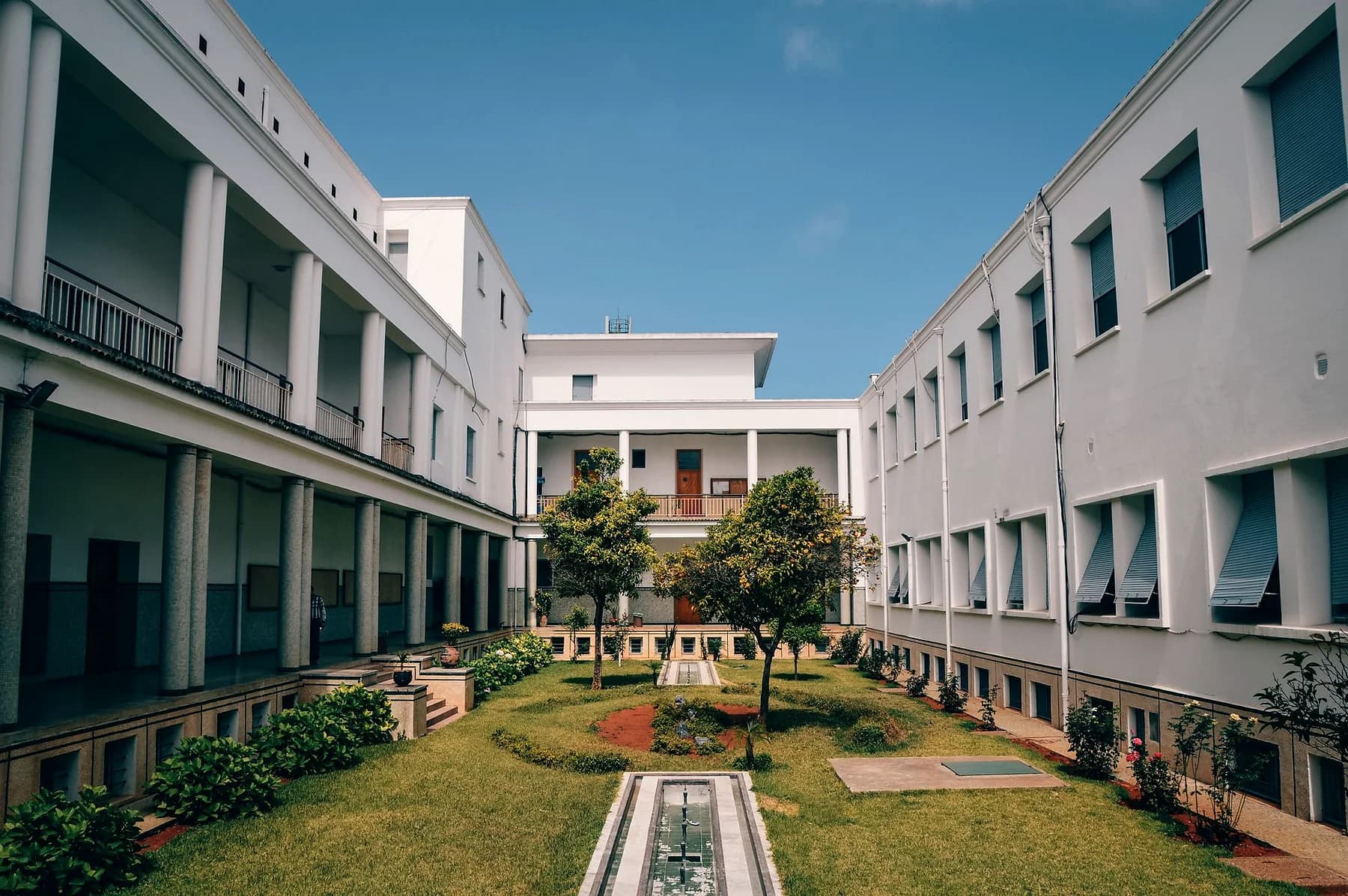 Courtyard of a low, colonnaded building with trees and lawn.